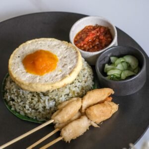 Vegan pesto fried rice topped with tofu egg, soy-based chickun skewer, served with pickles and sambal from Sauce Tree Bali